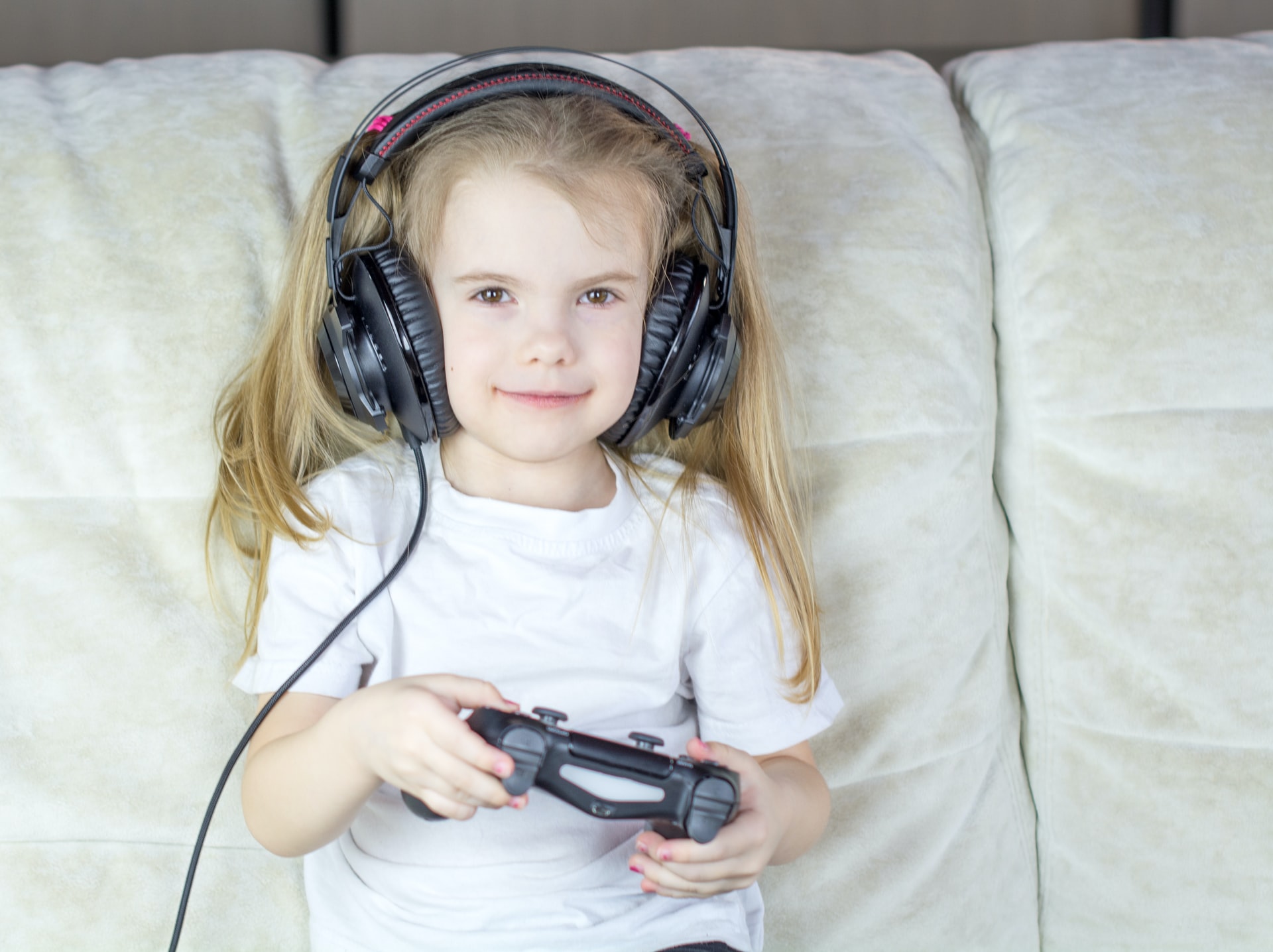 Jente med lyst langt hår sitter med headset i sofaen og gamer