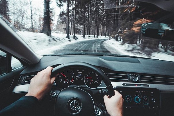 Ser to hender som holder på et ratt. Bilen kjører på veien og det er snø ved kantene.