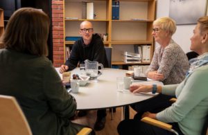 Fire voksne personer sitter rundt et bord og prater