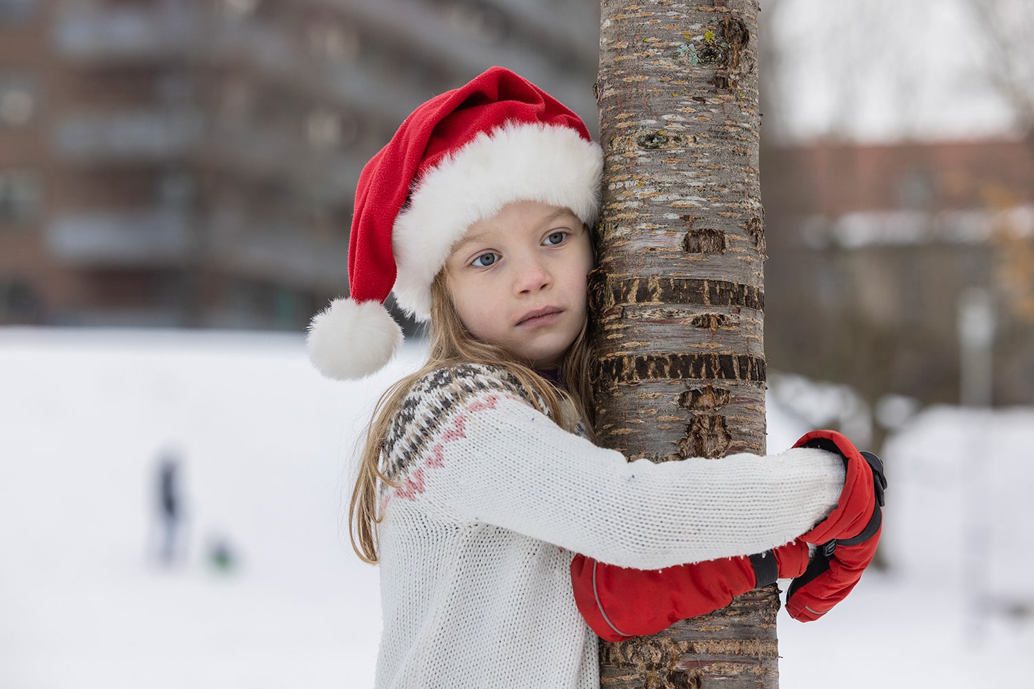 en liten jente med nisselue ser trist ut og holder rundt et tre