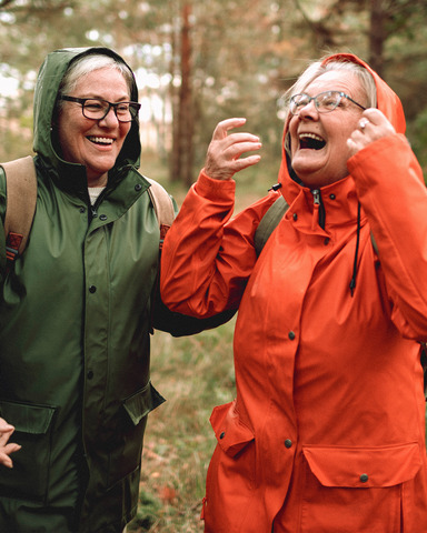 To glade damer på tur i skogen. Begge har på seg regntøy.