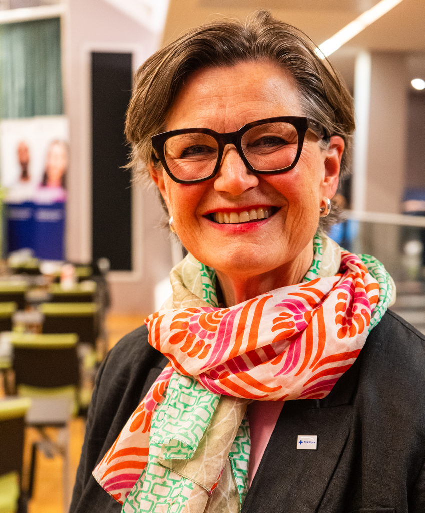 Bilde av lederen til Blå Kors landsstyret, Torbjørg Aalborg. Hun har mørkt hår og briller, dressjakke og et fargerikt skjerf rundt halsen.