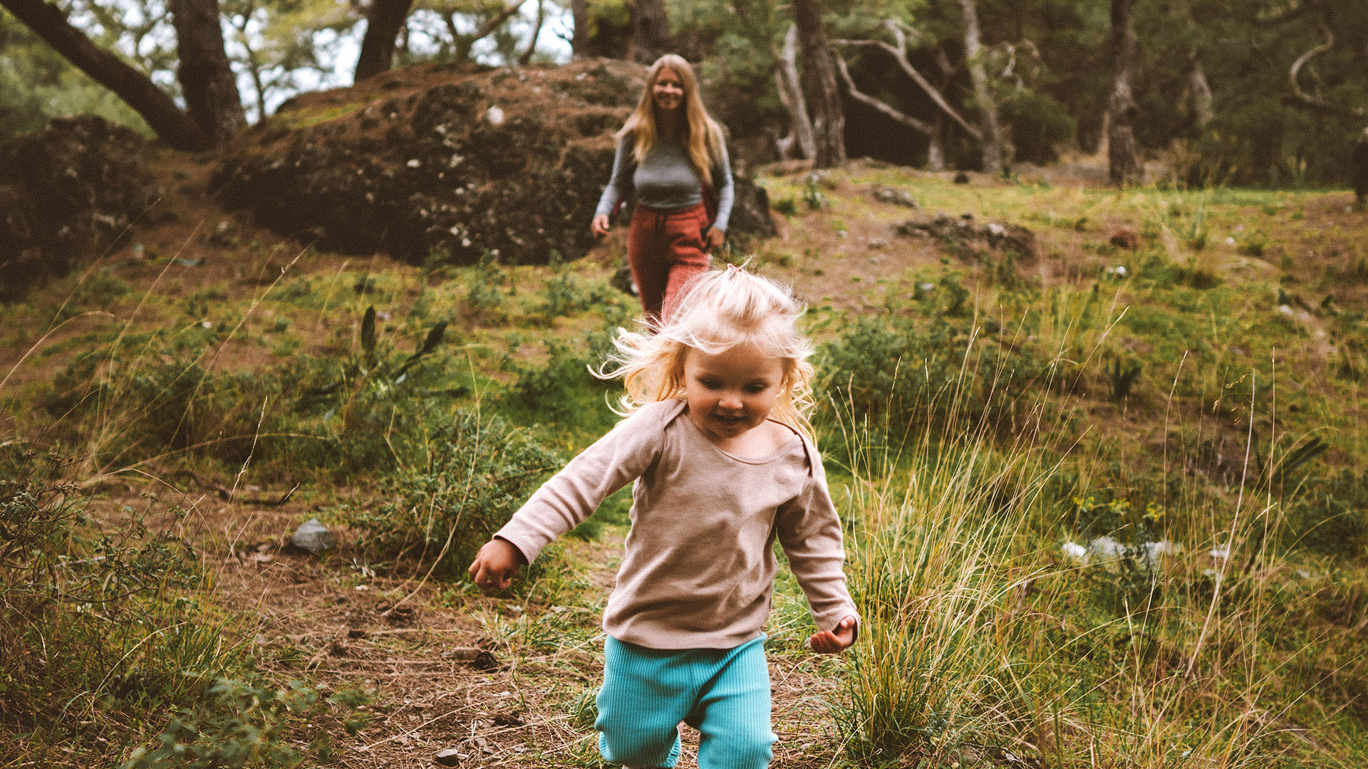 En liten jente er glad og løper i skogen. En voksen kvinne kommer etter