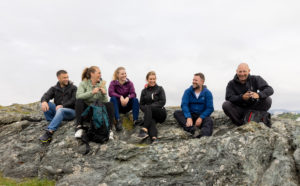 En gruppe på seks mennesker på tur ute. De sitter oppe på et fjell