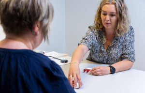 To kvinner sitter ovenfor hverandre. Dene kvinnen har klosser i hvitt og rødt og legger dem fram på bordet