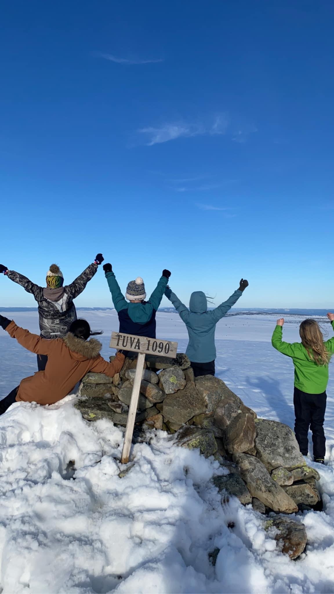 mennesker som reiser armene opp i glede på toppen av et fjell